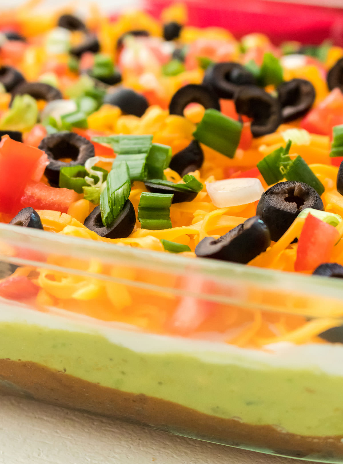 Closeup on a 9x13" glass baking dish filled with 7 layer dip sitting on a white table.