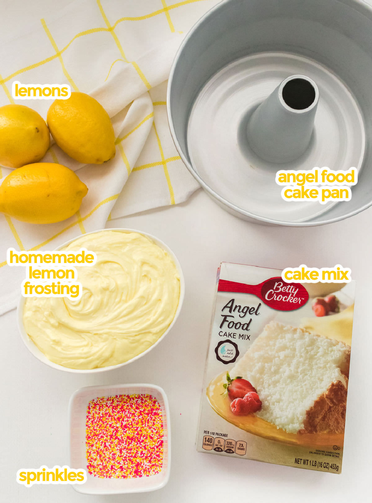 All the ingredients you will need to make Angel Food Cake with Lemon Frosting including an angel food cake pan, Angel Food Cake Mix, Lemon Frosting, lemons and sprinkles.
