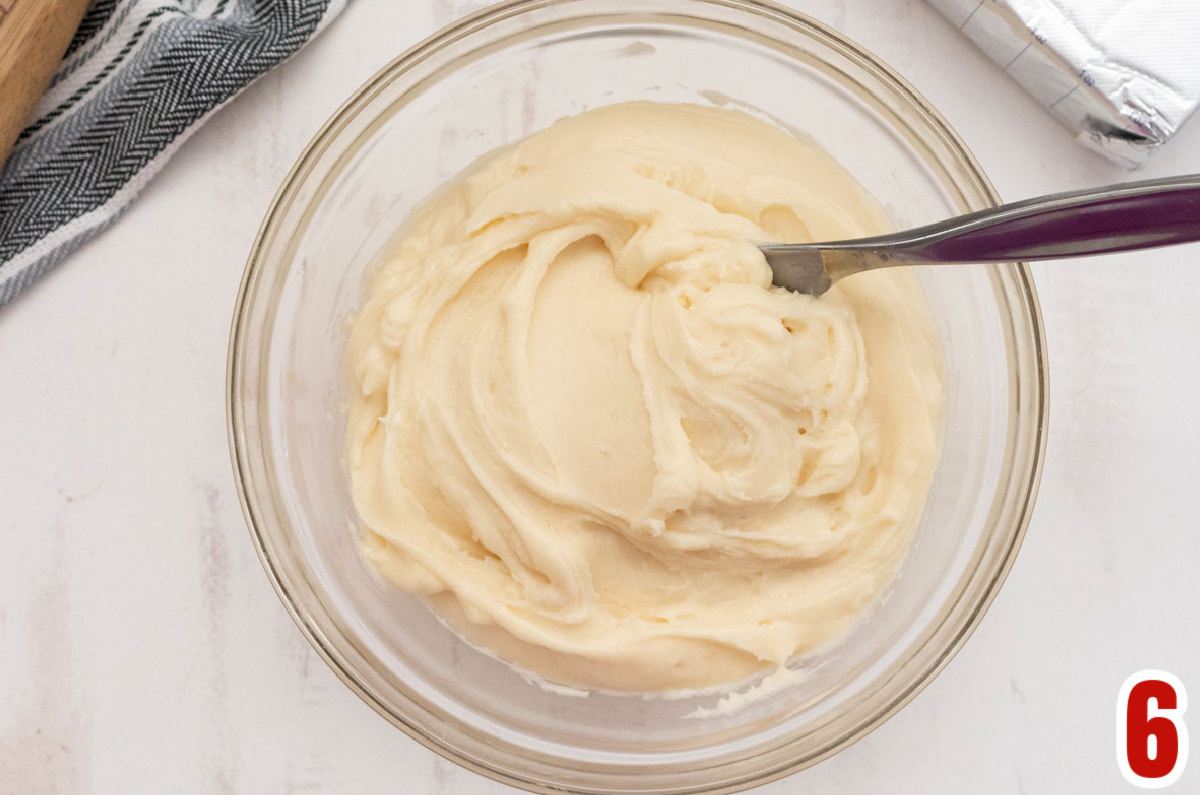 Closeup on a glass mixing bowl filled with homemade Cream Cheese Frosting and a knife.