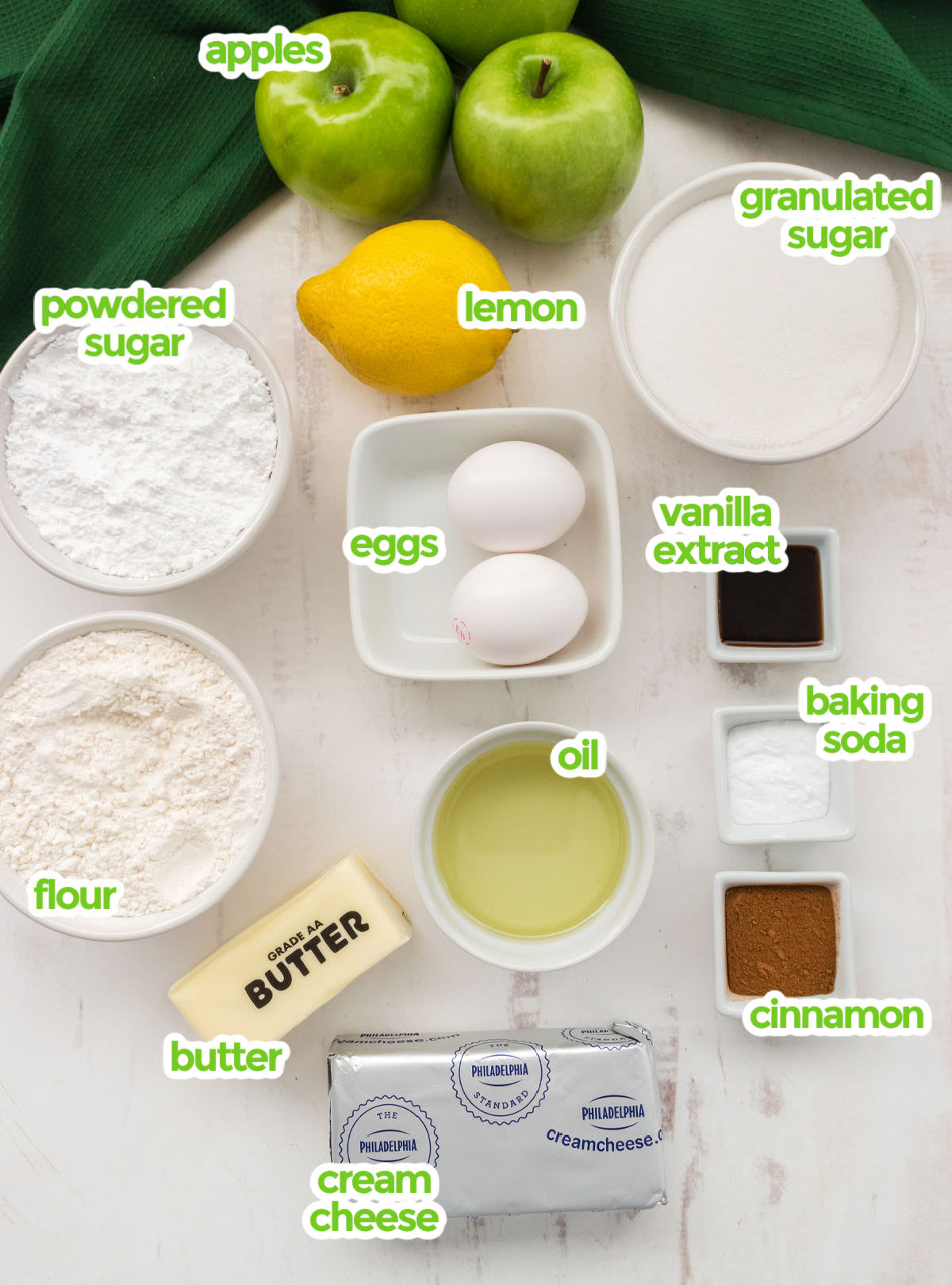 All the ingredients you will need to make Apple Cake including apples, lemon, granulated sugar, powdered sugar, eggs, vanilla extract, baking soda, cinnamon, oil, flour, butter and cream cheese.
