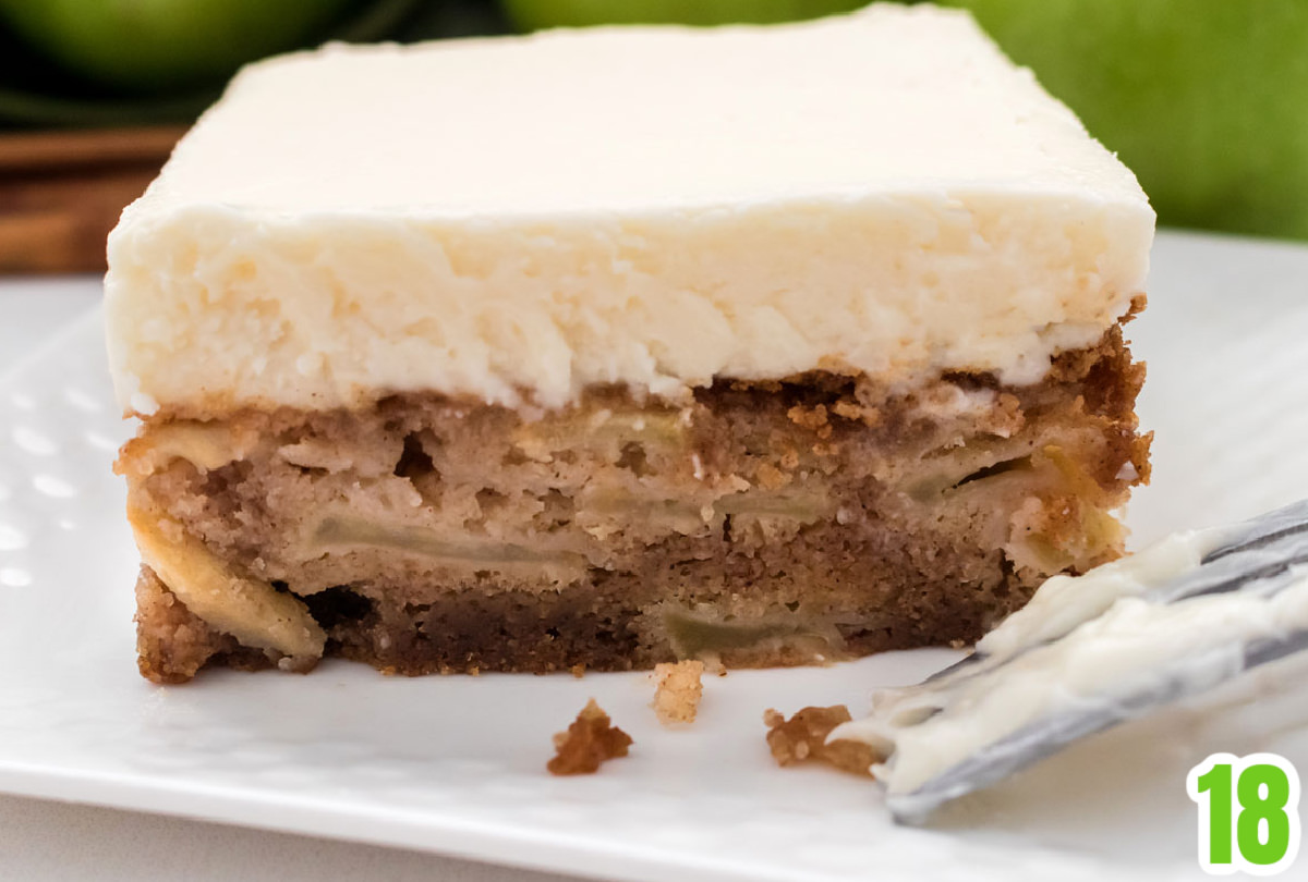 Closeup on a side view of a piece of Apple Cake showing the layers of apples in the cake and the think layer of Cream Cheese Frosting.