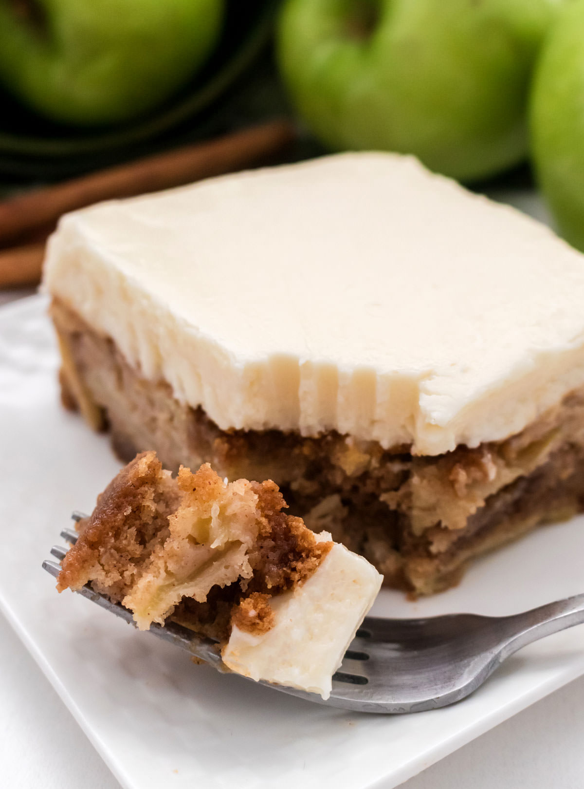 Closeup of a piece of Apple Cake sitting on a white plate with a bite on a fork.