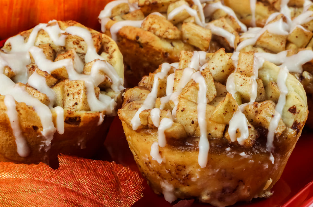 Closeup on four Easy Apple Cinnamon Rolls sitting on a red serving platter surrounded by Fall leaves.