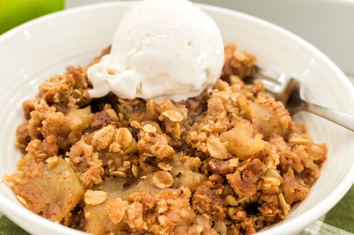 Closeup on a white bowl filled with Easy Apple Crisp topped with a scoop of Vanilla Ice Cream sitting on a green kitchen towel.