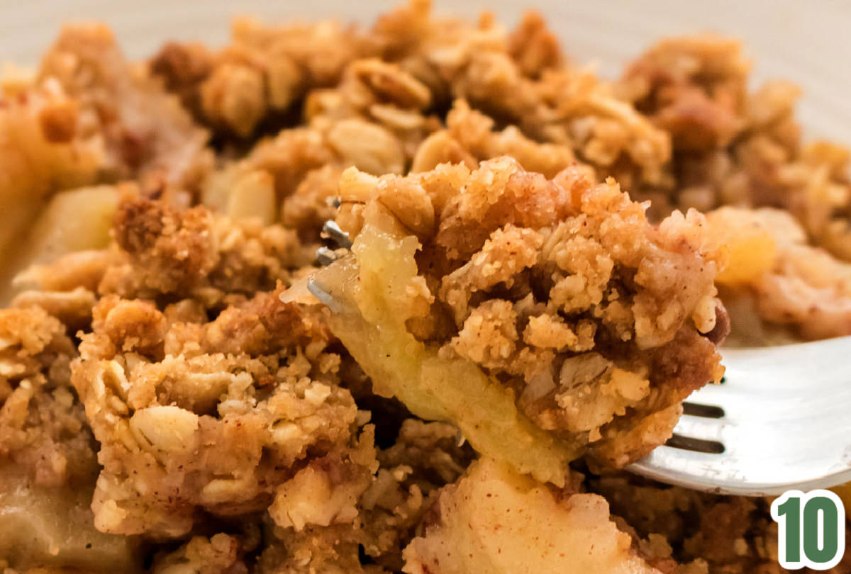 Closeup on a bowl of Apple Crisp with a fork in the foreground filled with a bite of the dessert.
