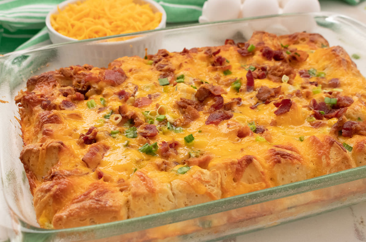Close up of a Bacon and Egg Breakfast Casserole in a glass baking pan sitting in front of a ramekin of cheese and a bowl of eggs.