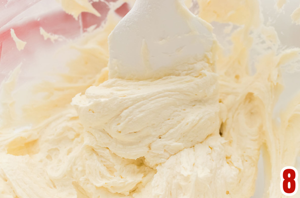 Closeup on a glass mixing bowl filled with Baileys Irish Cream icing and a white spatula.