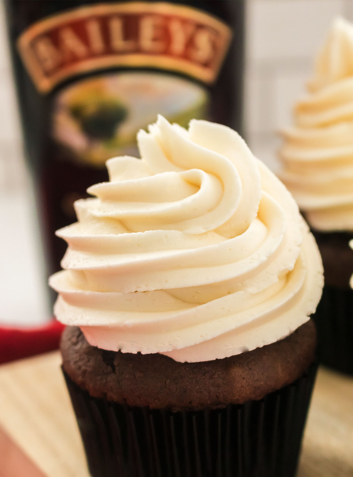 Closeup on a chocolate cupcake topped with Baileys Irish Cream Buttercream Frosting sitting in front of a bottle of Baileys Irish Cream Liqueur 