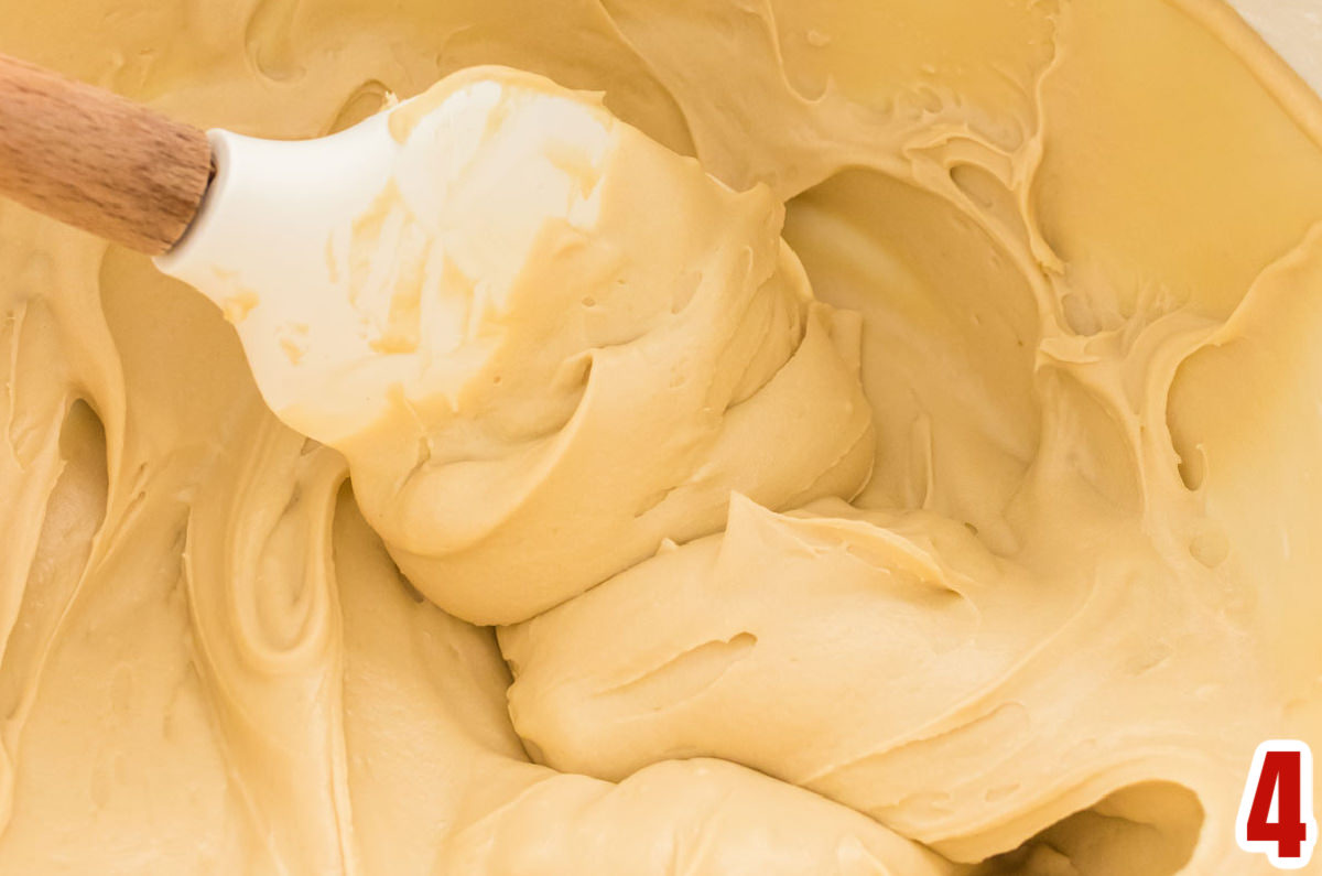 Closeup on a white mixing bowl filled with Brown Sugar Cream Cheese Frosting and a white wooden spatula.