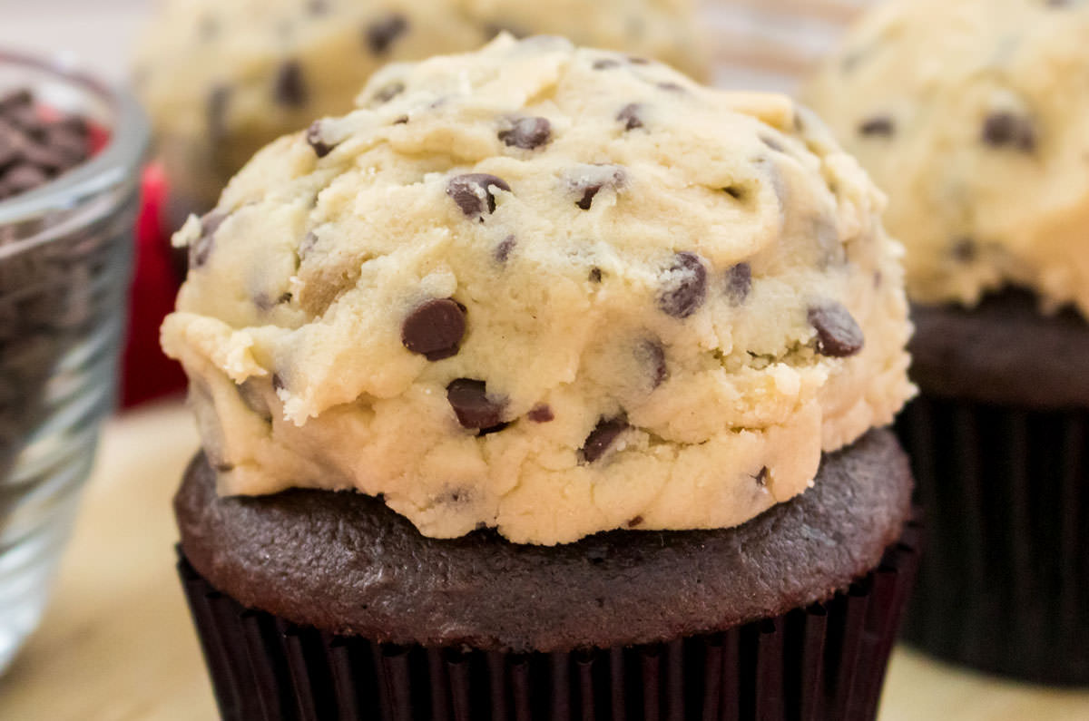 Closeup on three cupcakes frosted with The Best Cookie Dough Frosting sitting next to a ramekin filled with Mini Chocolate Chips.