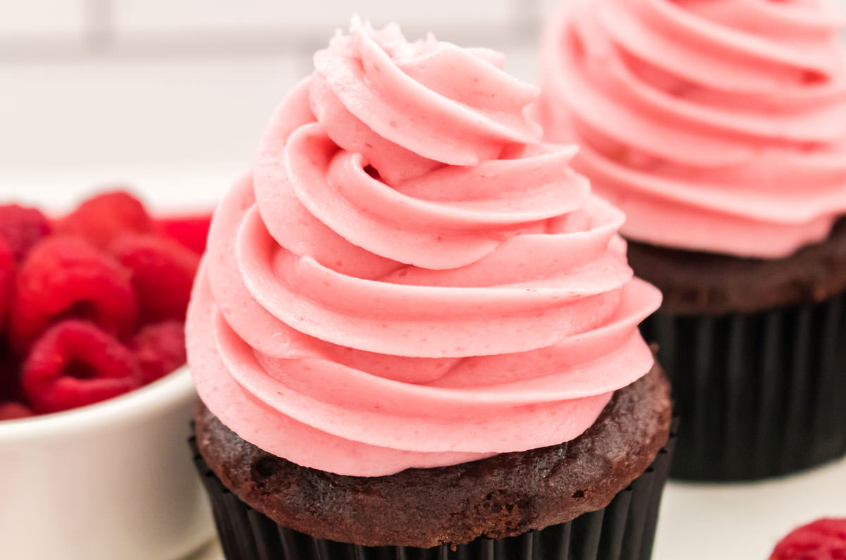 Closeup on two chocolate cupcakes topped with swirls of The Best Raspberry Frosting.
