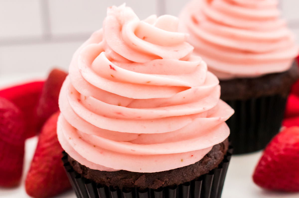 Closeup on two cupcakes topped with a swirl of The Best Strawberry Buttercream Frosting.