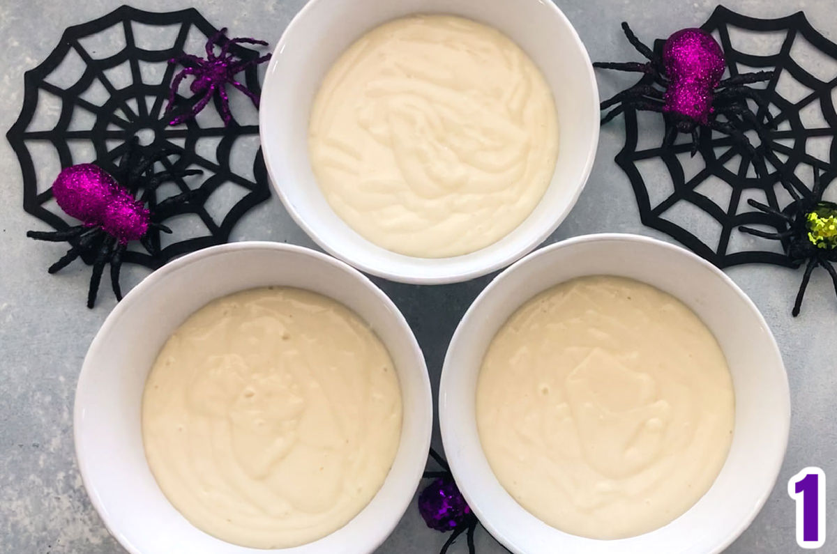 Closeup of three bowls filled with cake batter sitting on a grey surface.