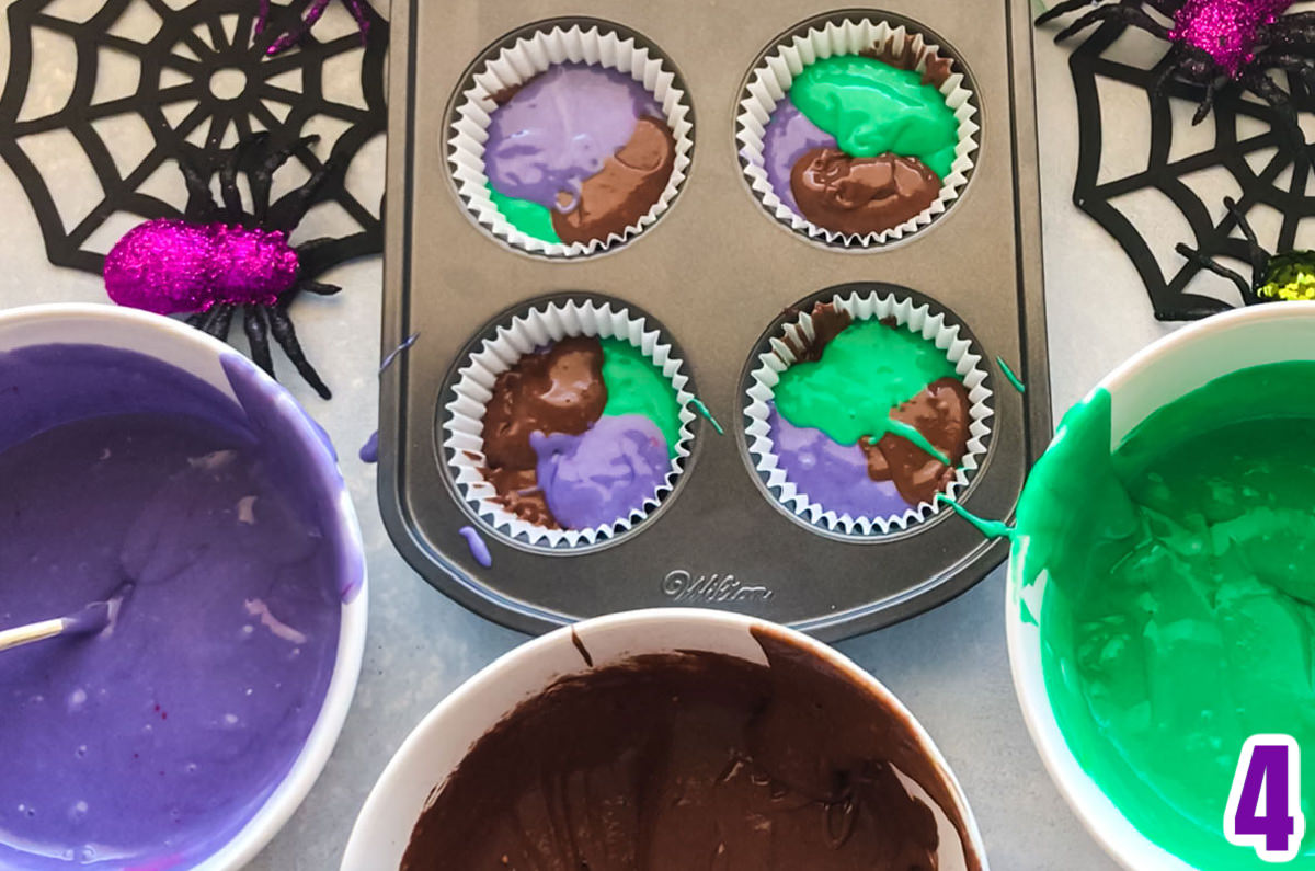 Cupcake tin filled with marble cupcake batter surrounded by bowls of purple, chocolate and green cake batter.
