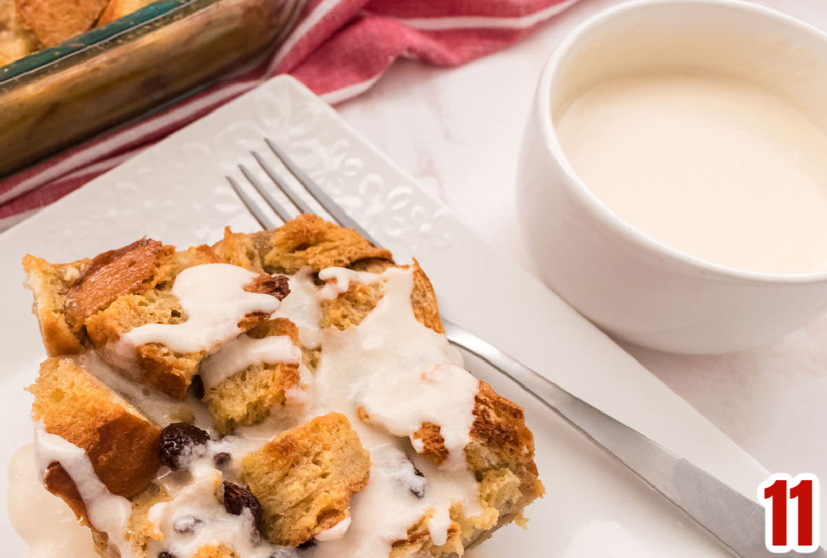 A small white bowl of Vanilla Sauce sitting next to a piece of Bread Pudding on a white plate.