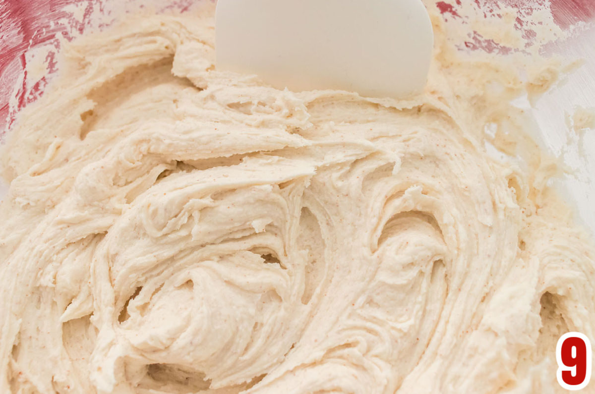 Closeup on a batch of Brown Butter Frosting in a clear mixing bowl with a white spatula.