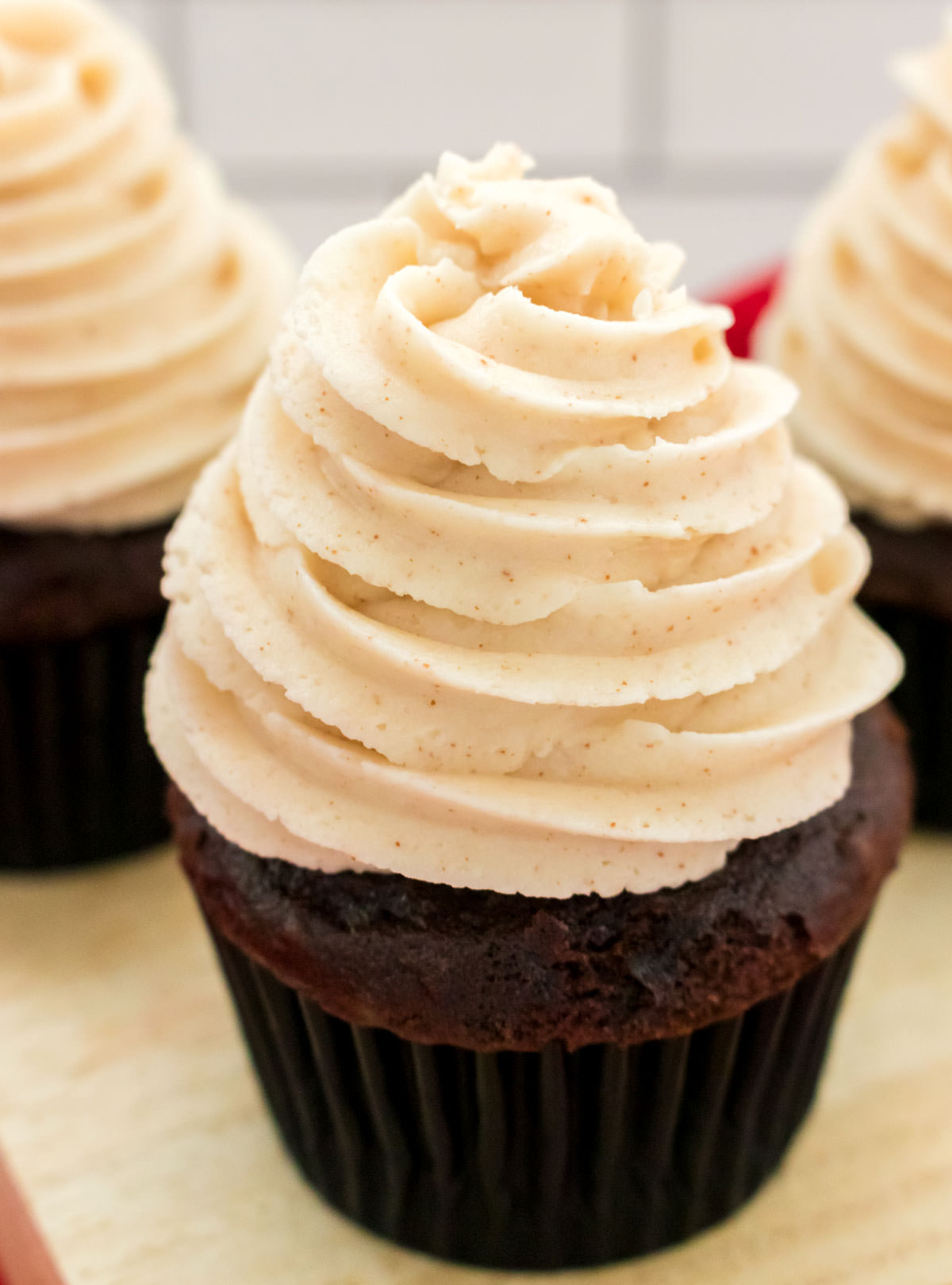 Closeup on three cupcakes topped with Brown Butter Buttercream Frosting sitting on a cutting board.