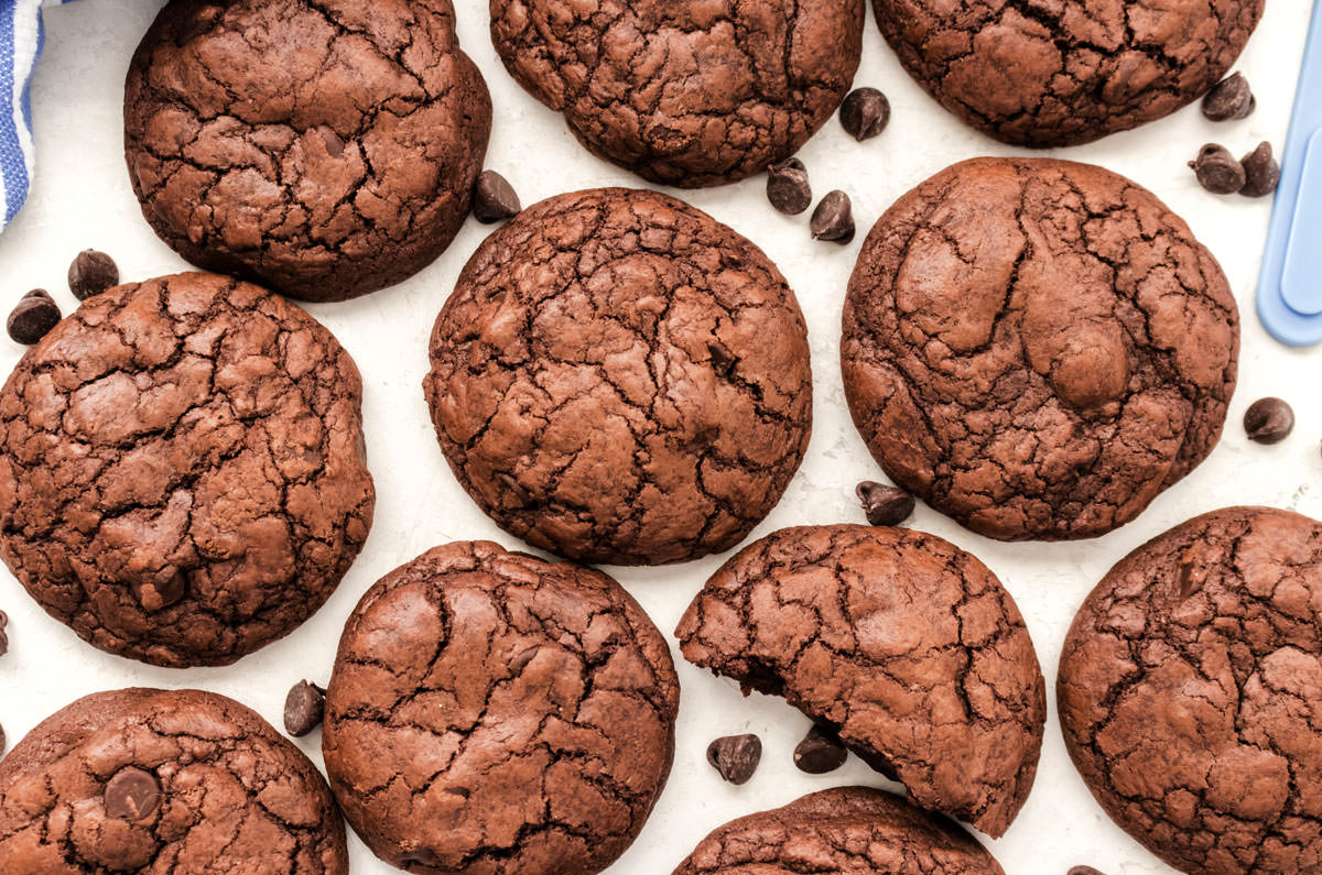A batch of The Best Ever Brownie Cookies laying on a white table surrounded by chocolate chips.