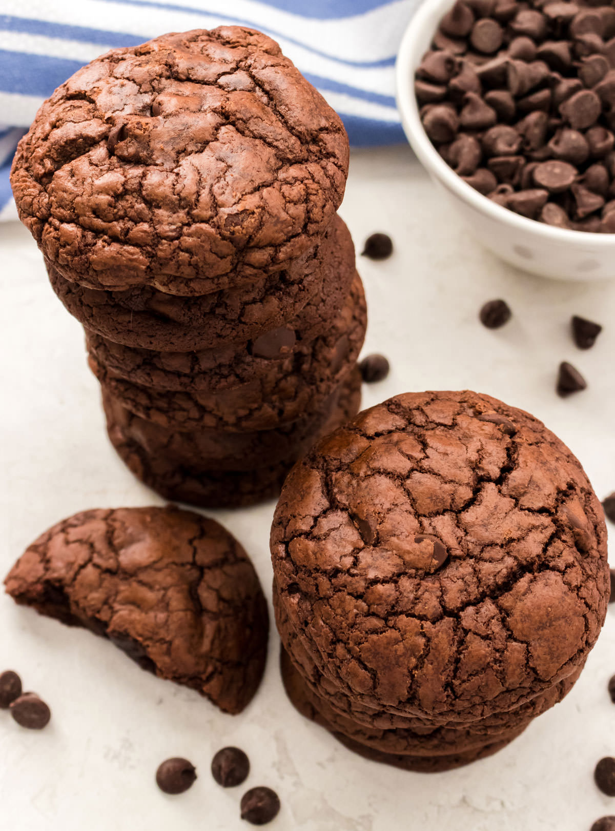 Closeup on two stacks of Brownie Cookies sitting on a white table in front of a bowl of chocolate chips.