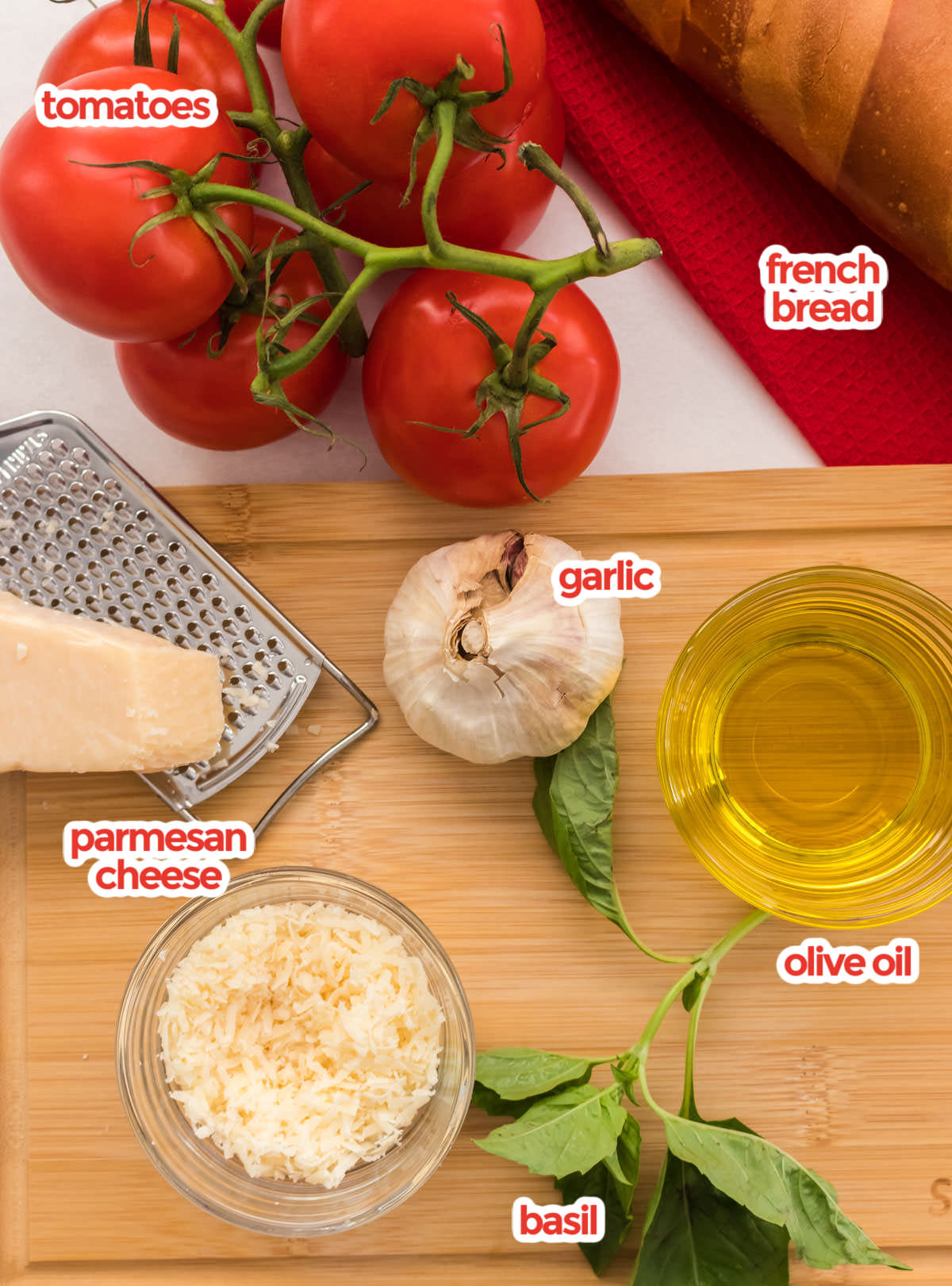 Italian Bruschetta recipe ingredients on a table including red tomatoes, garlic, parmesan cheese, oil and more.