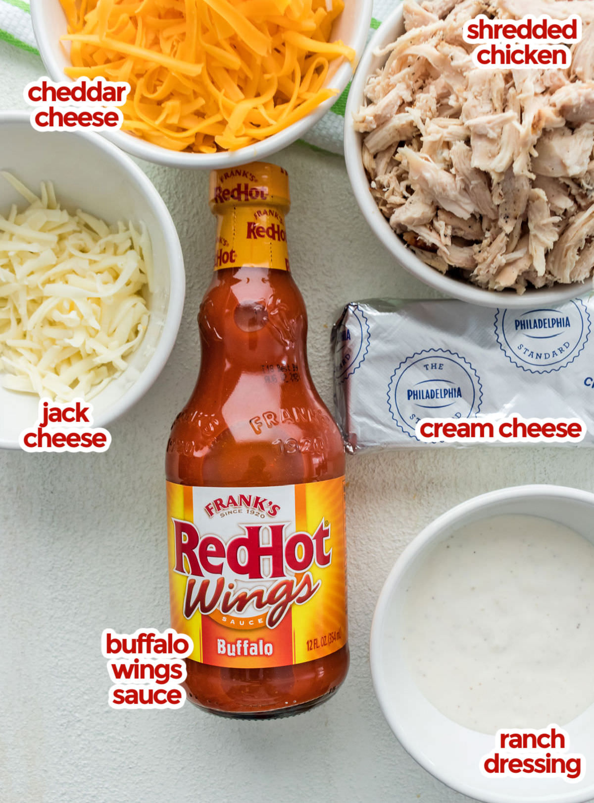 All the ingredients you will need to make Buffalo Chicken Dip including shredded chicken, cheddar cheese, jack cheese, cream cheese, ranch dressing and buffalo wings sauce.
