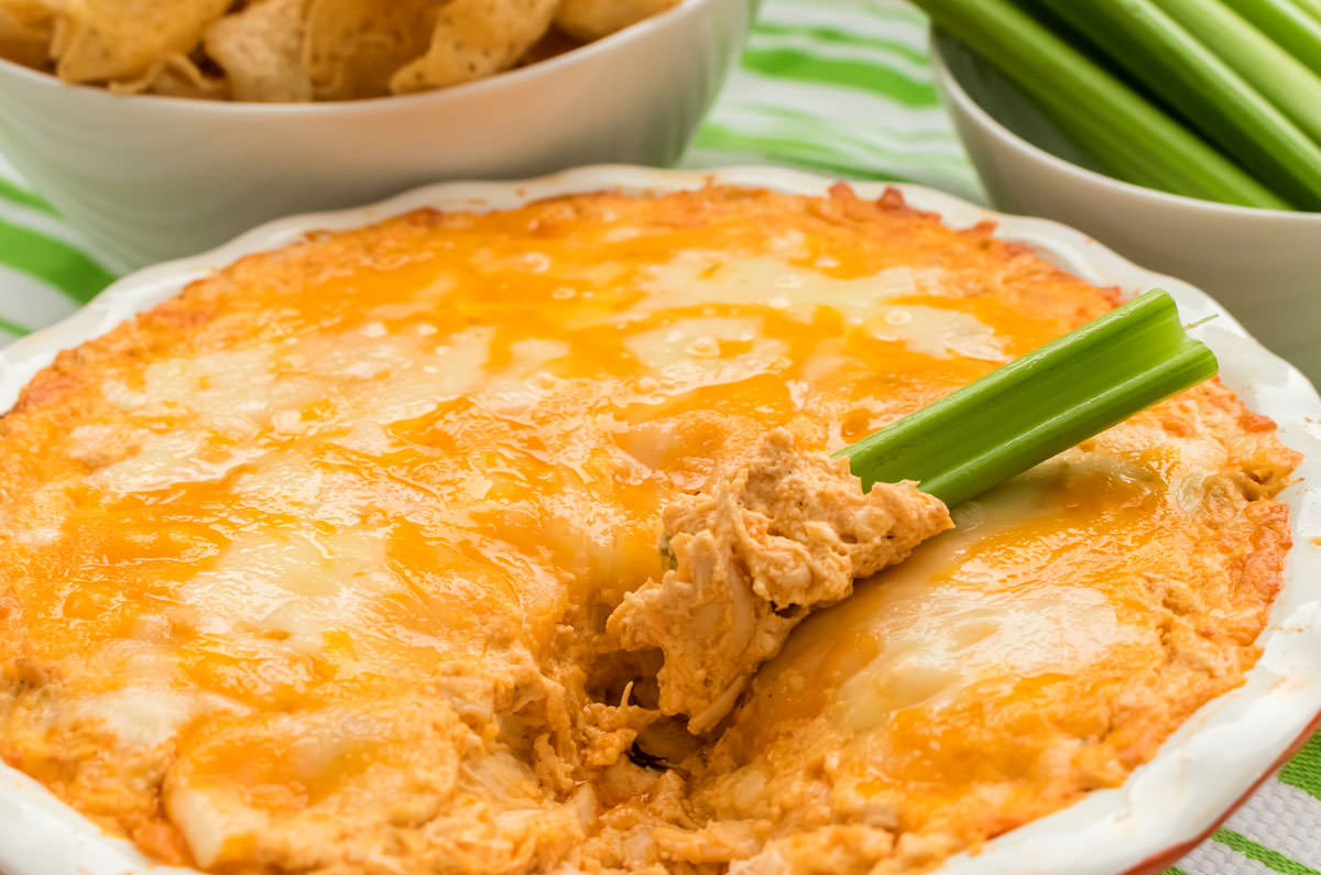 Close up of a round ceramic pie plate filled with Buffalo Chicken Dip covered in melted cheese. 