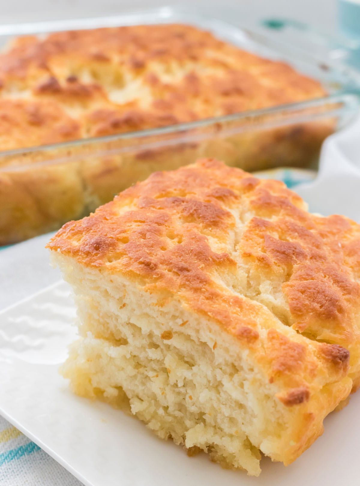 Closeup on a Butter Swim Biscuit sitting on a white plate in front of the pan of Butter Dip Biscuits.