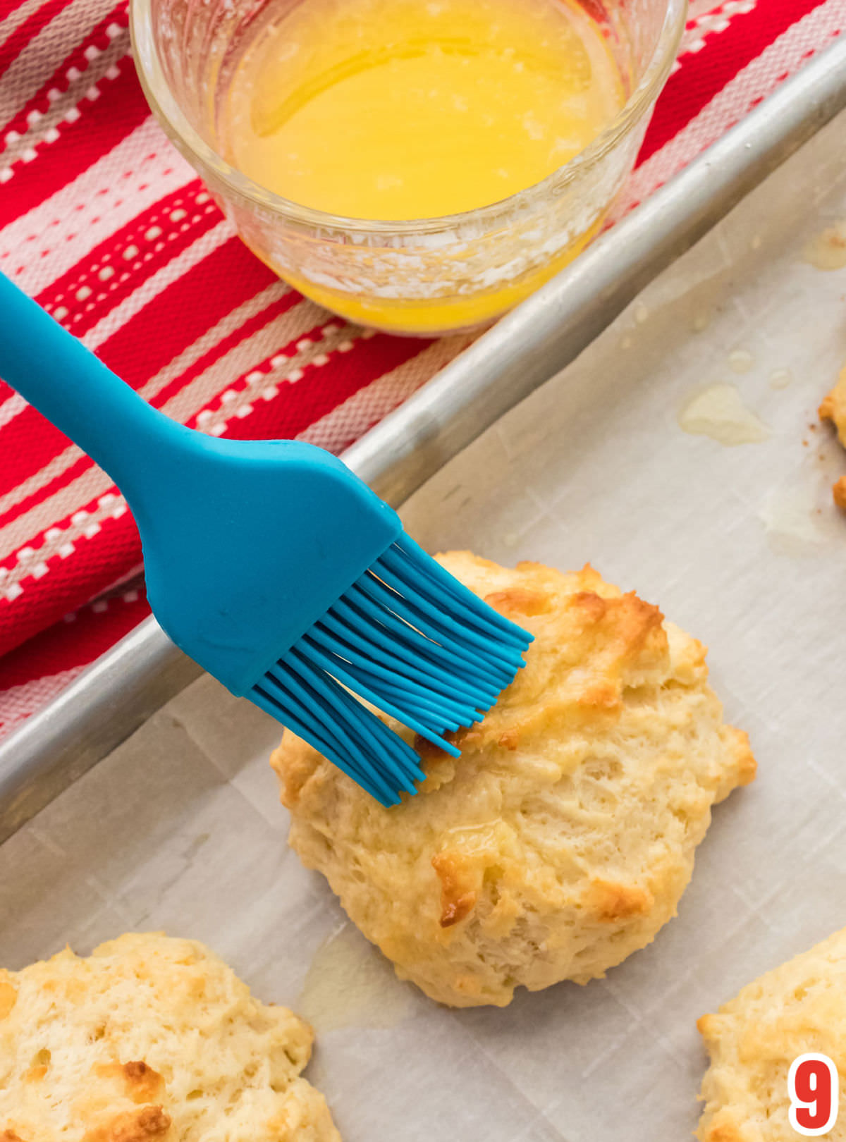 Closeup on a blue pastry brush brushing melted butter on the Drop Biscuits that just came out of the oven.