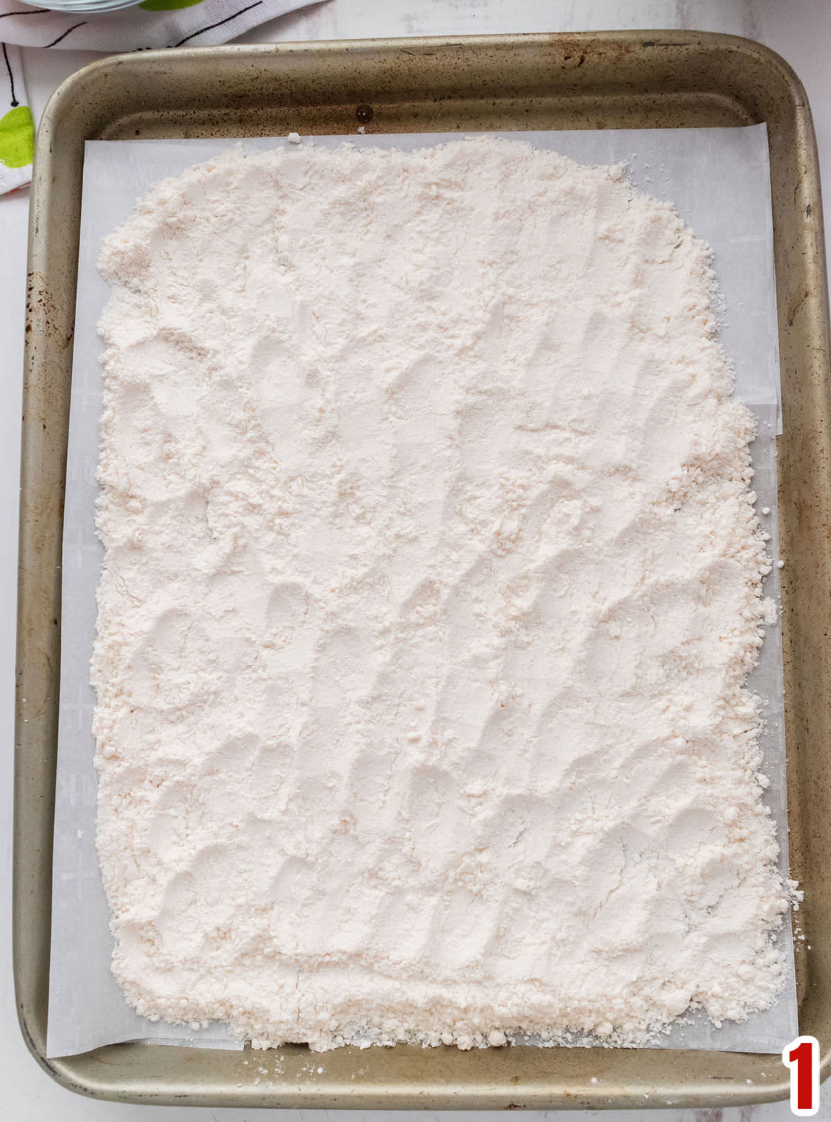 Closeup on a cookie sheet covered with a layer of yellow cake mix.