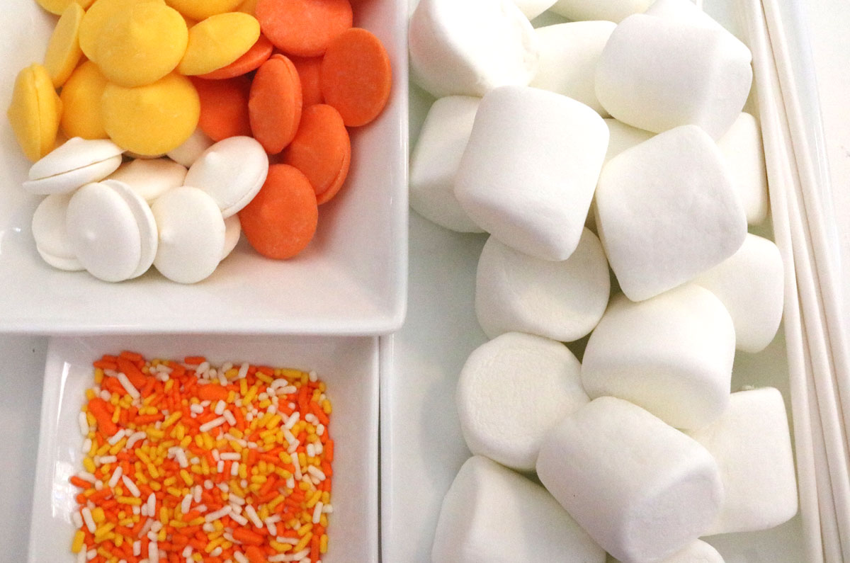 All the ingredients you will need to make Candy Corn Marshmallow Pops including Candy Melts, Marshmallows, Lollipop sticks and Halloween Sprinkles.