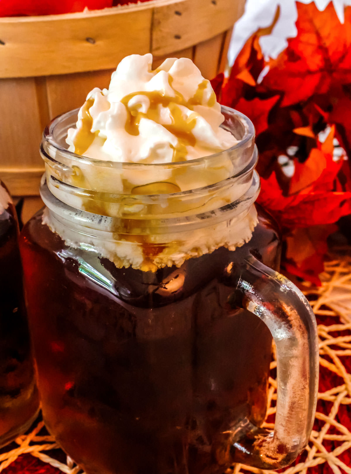 Closeup on a glass mug filled with Caramel Apple Cider topped with Whipped Cream and Caramel sauce.