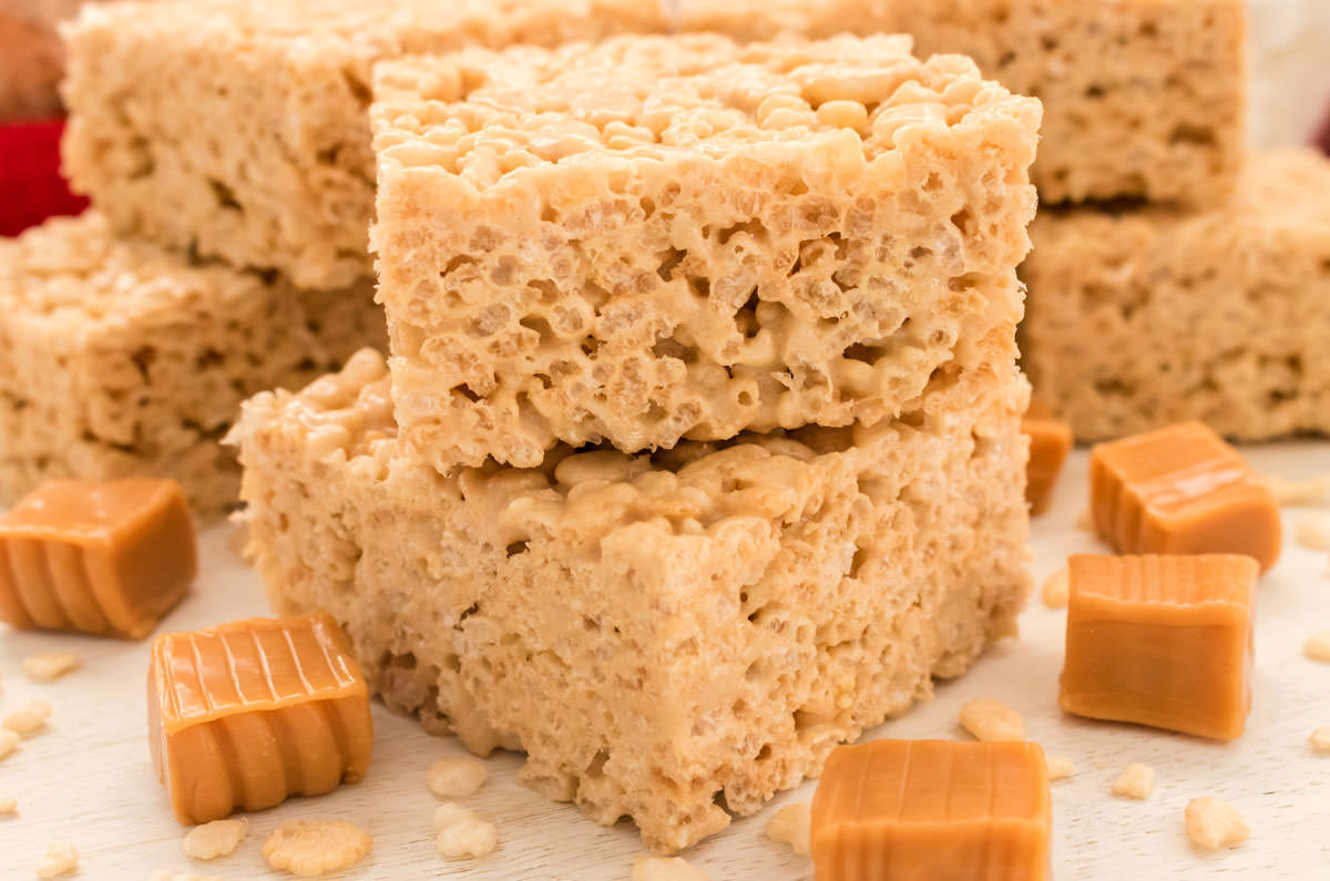 Closeup on stacks of Caramel Rice Krispie Treats sitting on a white table surrounded by Caramel Candies.