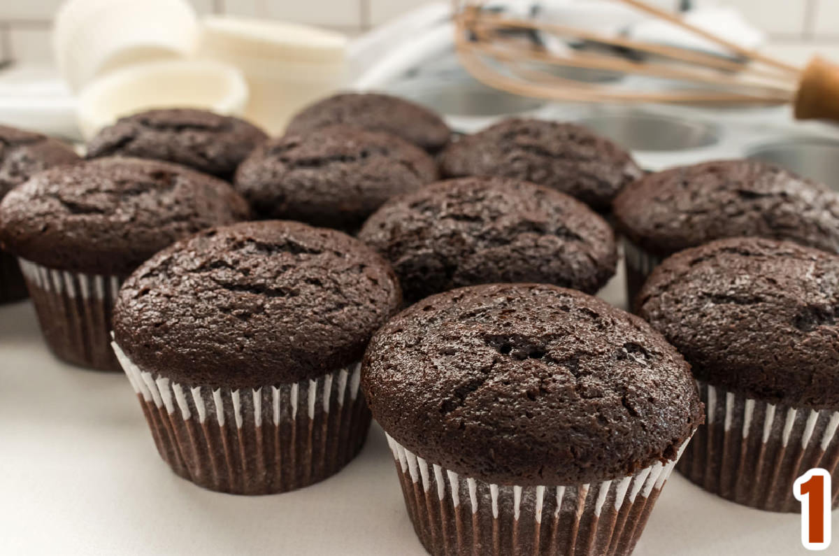 Closeup on a dozen chocolate cupcakes sitting on a white table.