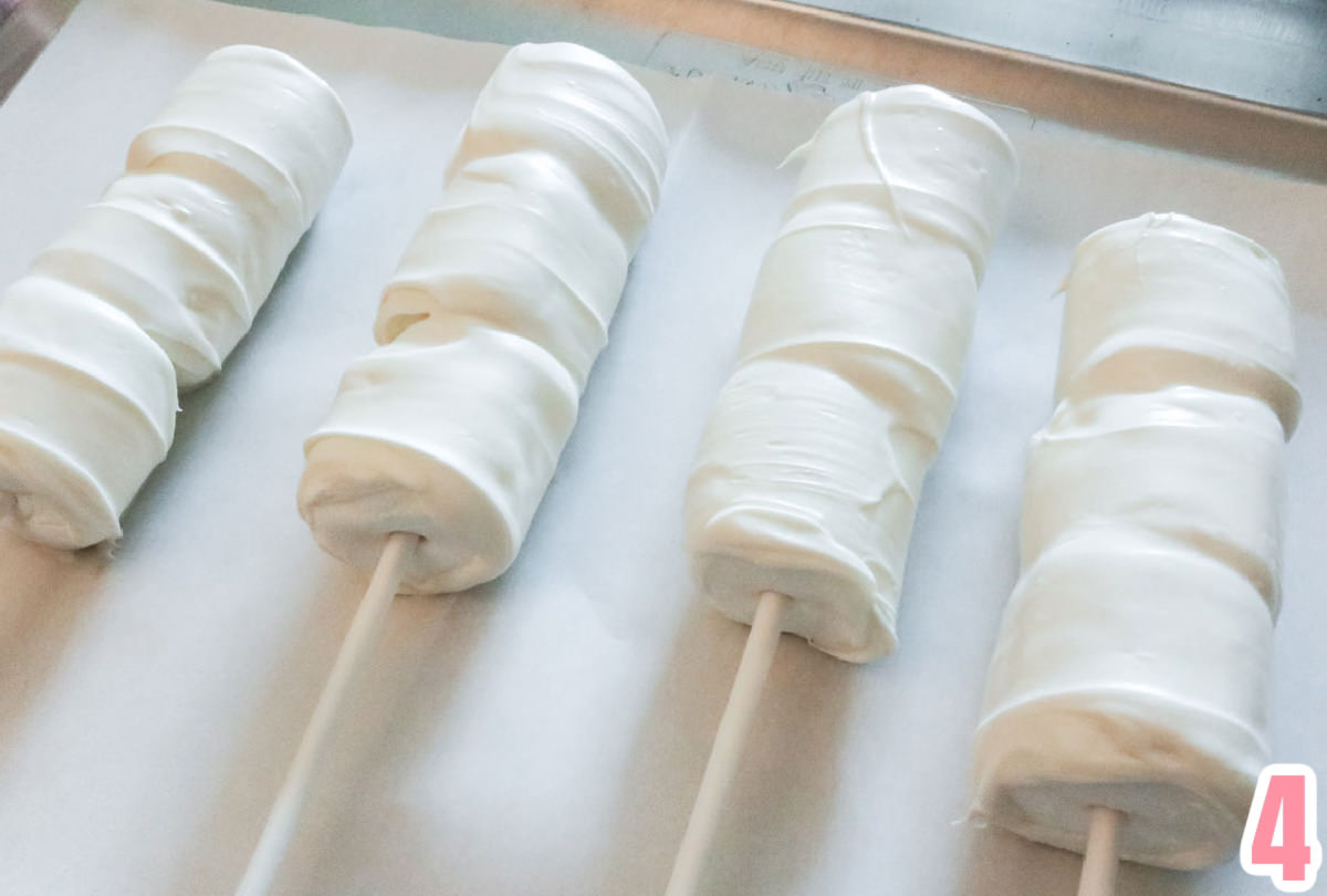Four marshmallow pops covered in white chocolate drying on a parchment paper covered cookie sheet.