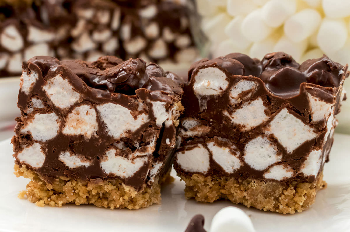 Closeup on two Chocolate Marshmallow Bars sitting on a white table in front of a bowl of mini marshmallows.