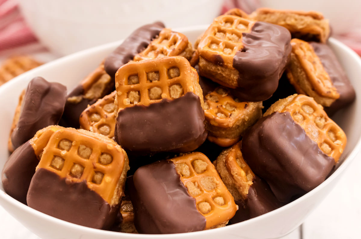 Closeup on a white serving bowl filled with Chocolate Peanut Butter Pretzel Bites sitting on a white table in front of another white bowl.