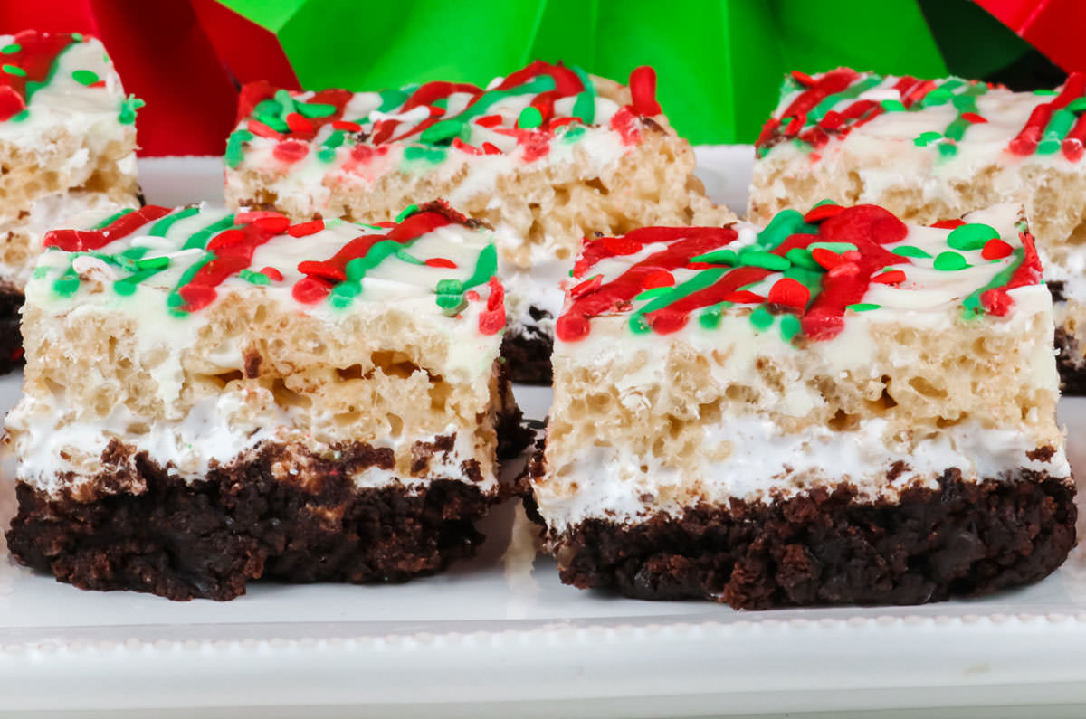 Closeup on a batch of Christmas Brownie Rice Krispie Treats laying on a white serving platter in front of Red and Green Christmas decorations.