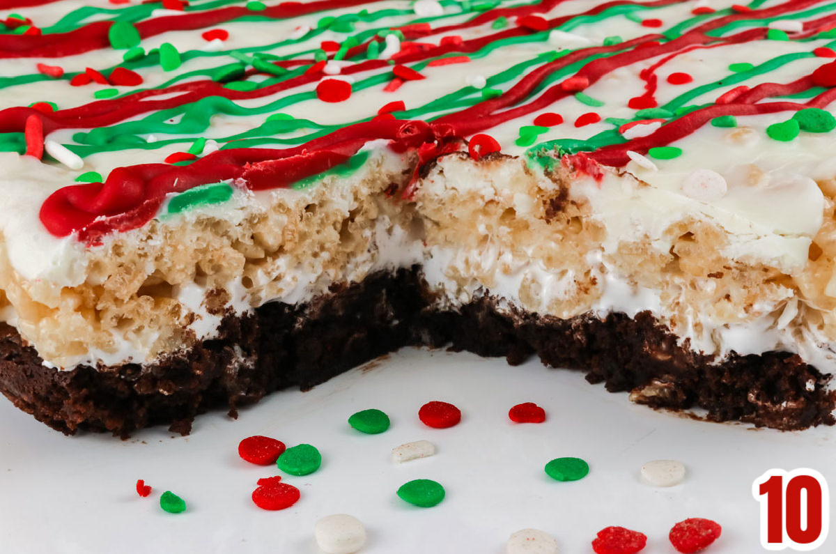 Closeup on a batch of Christmas Brownie Rice Krispie Treats sitting on a white surface with a single piece removed.
