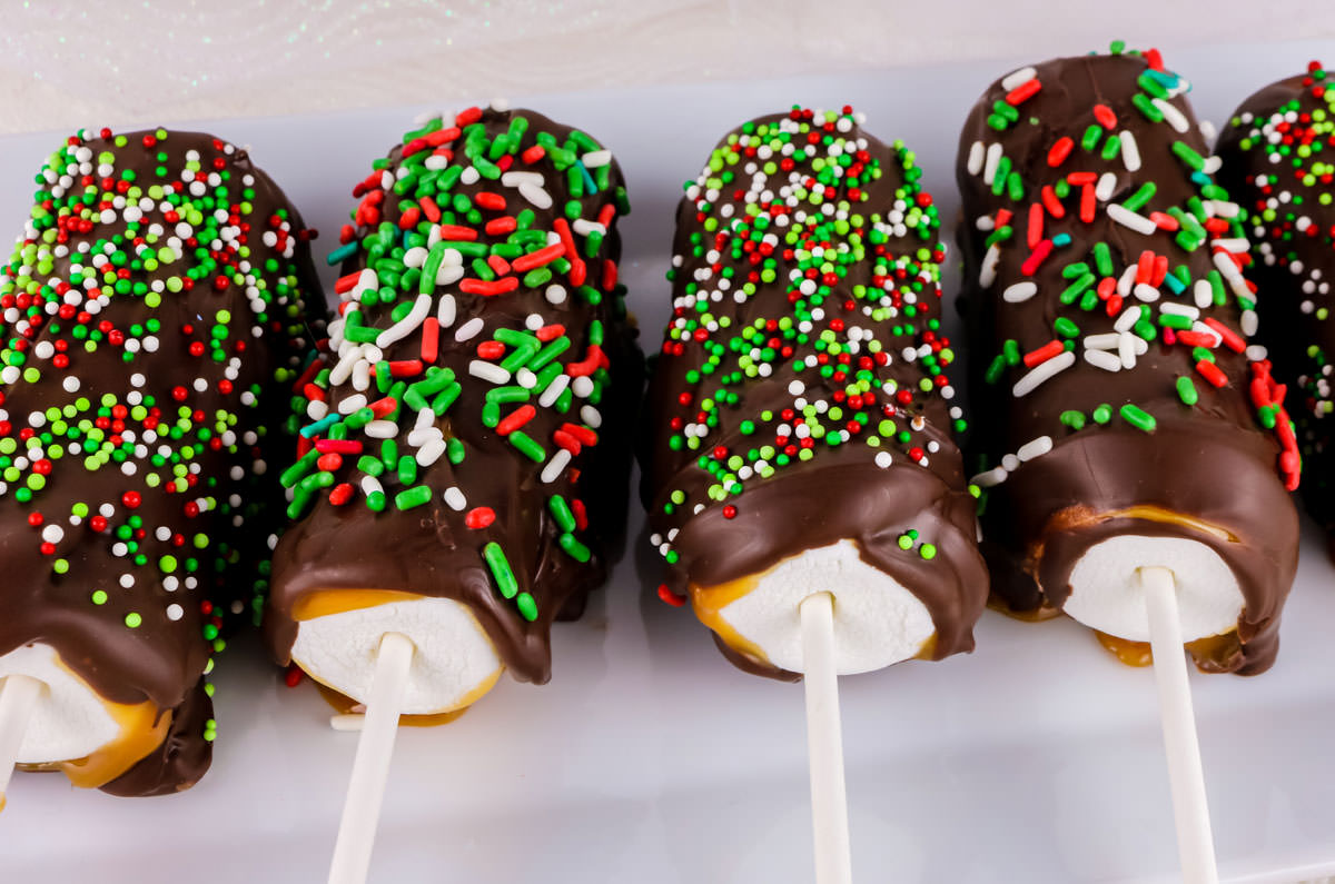 Five Christmas Caramel Marshmallow Pops on a white dish on a white table.