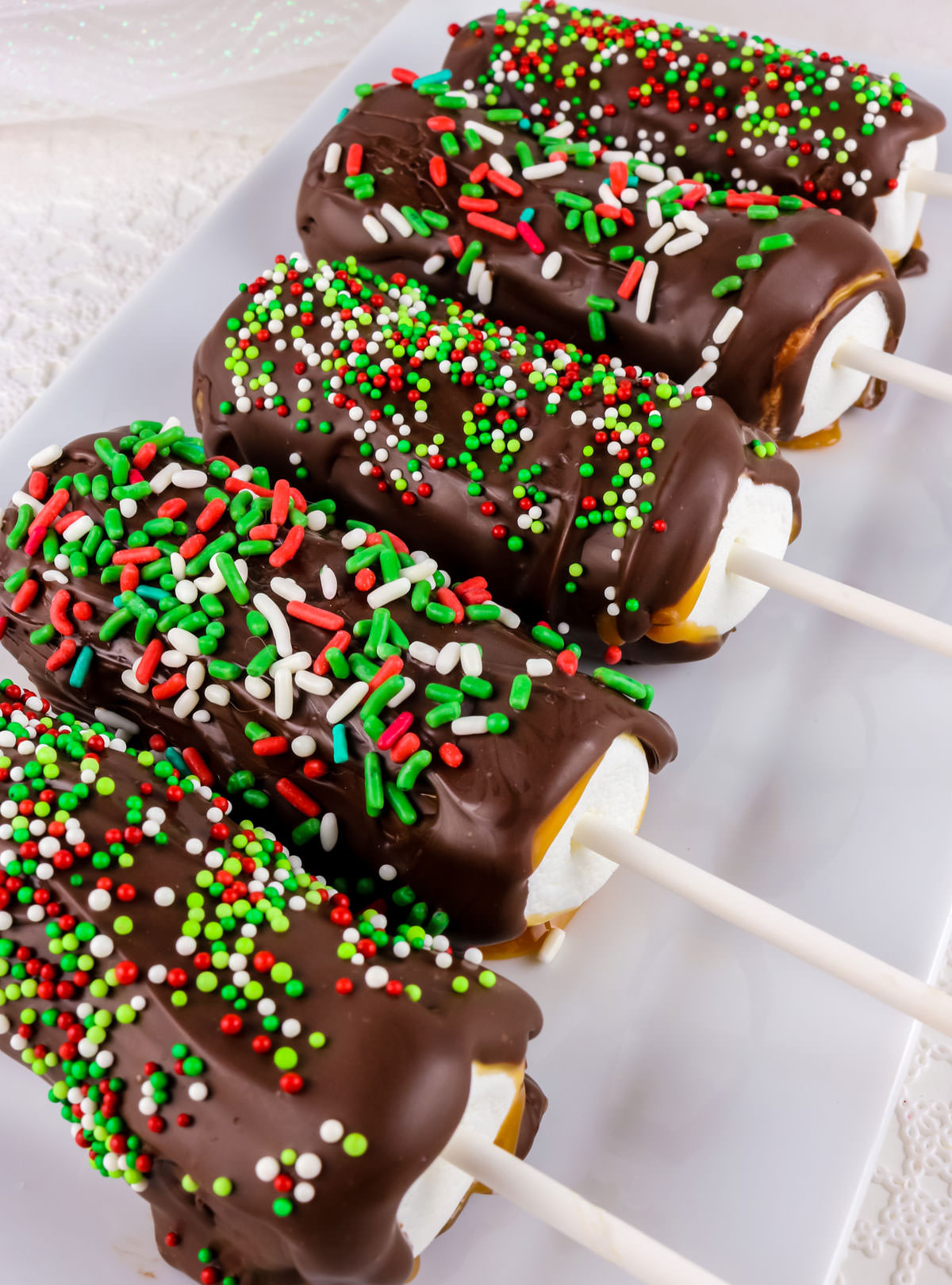 Closeup on five Christmas Caramel Marshmallow Pops laying on a white serving platter.