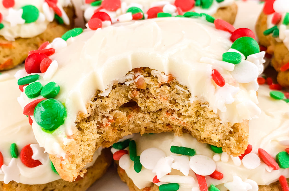 Closeup on a batch of Christmas Carrot Cake Cookies frosted with Cream Cheese Frosting, one with a big bite taken out of it.