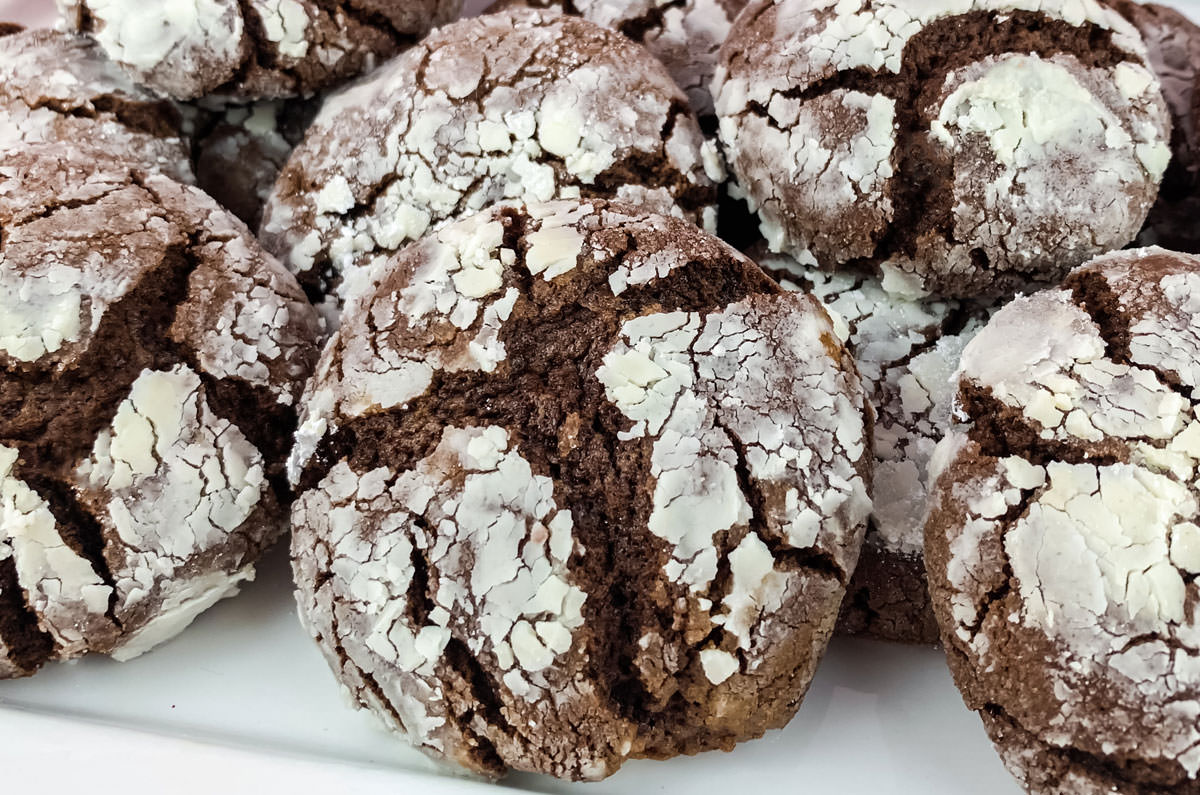 Closeup on a batch of Chocolate Crinkle Cookies sitting on a white serving plate.
