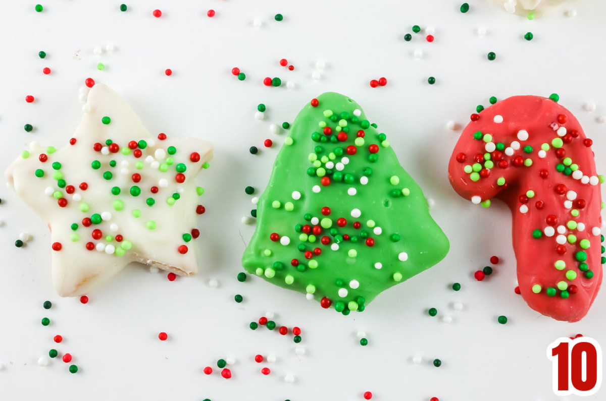 Three Red, Green and White Christmas Circus Animal Cookies laying on a white table surrounded by Holiday sprinkles.