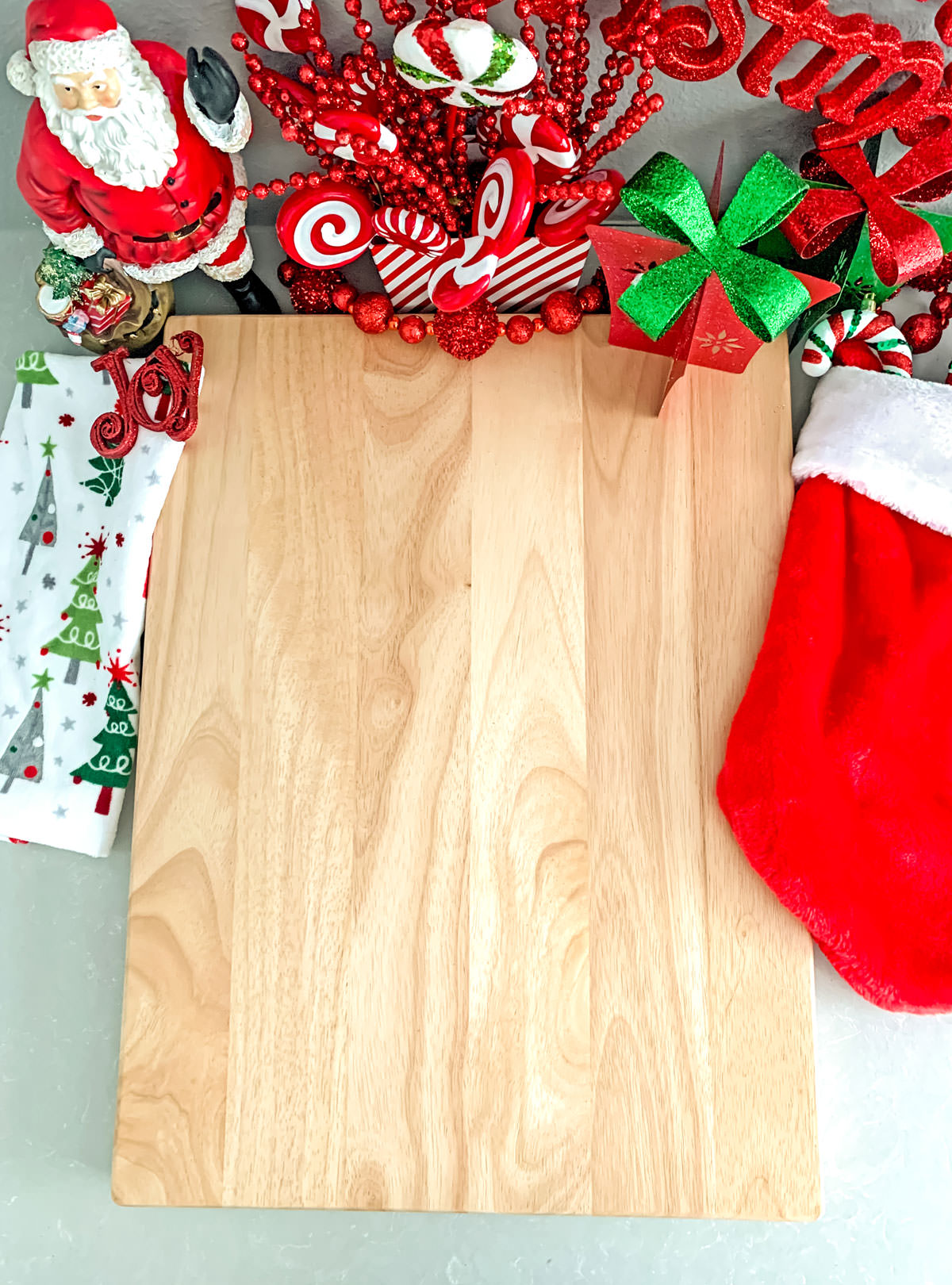 Closeup of a large wooden cutting board surrounded by a Christmas stocking, a Christmas kitchen towel and Christmas decorations.