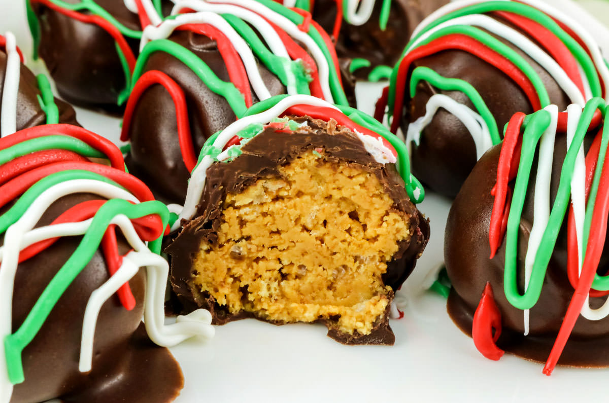 Closeup on a batch of Christmas Peanut Butter Crunch Truffles on a white plate, the one in the center is cut in half.