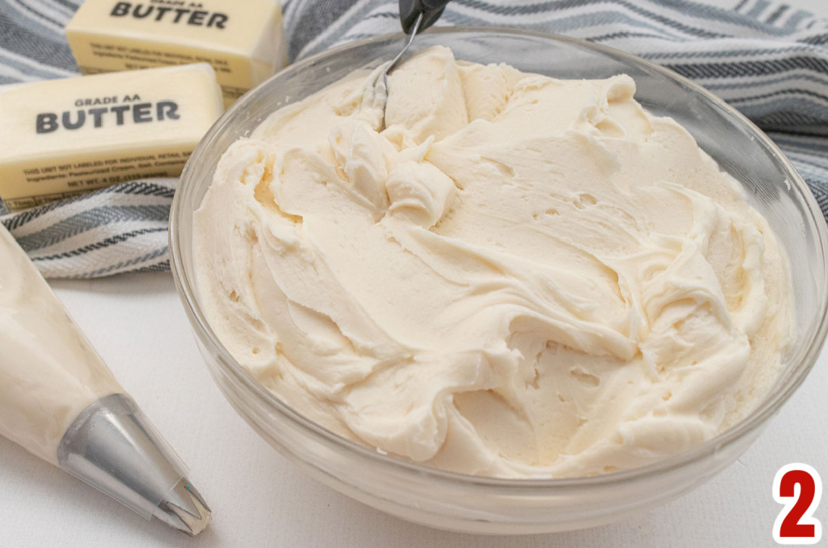 Closeup on a glass bowl filled with Buttercream Frosting sitting on a white table.