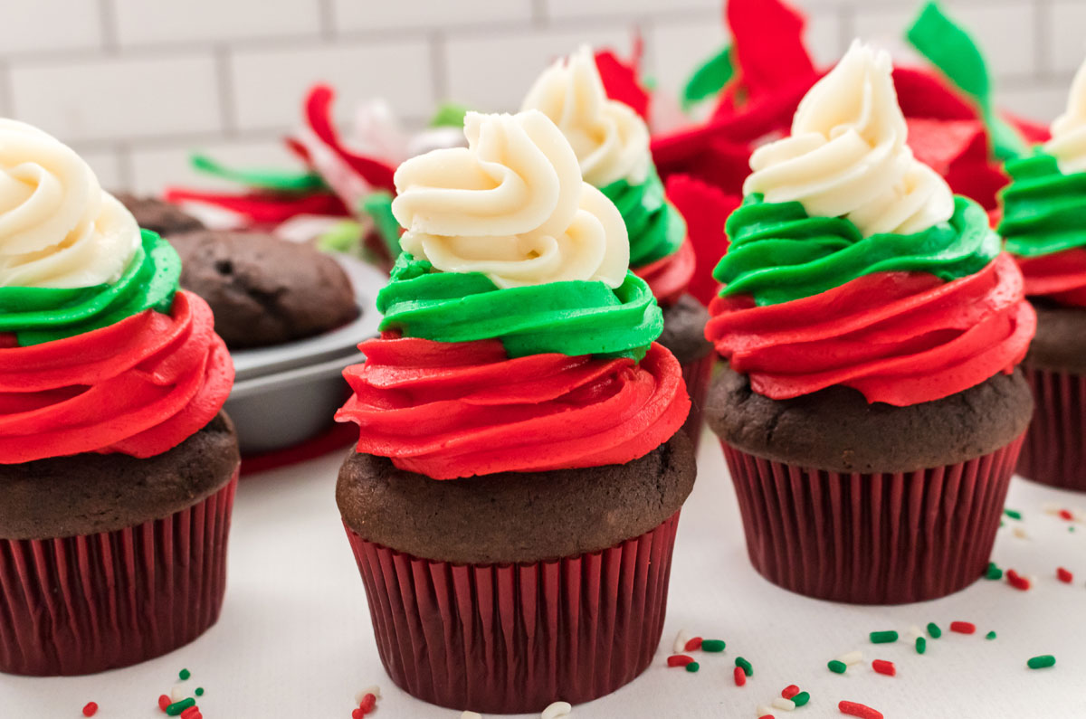 Closeup on five Easy Christmas Cupcakes sitting on a white table surrounded by Christmas sprinkles and Christmas decorations.