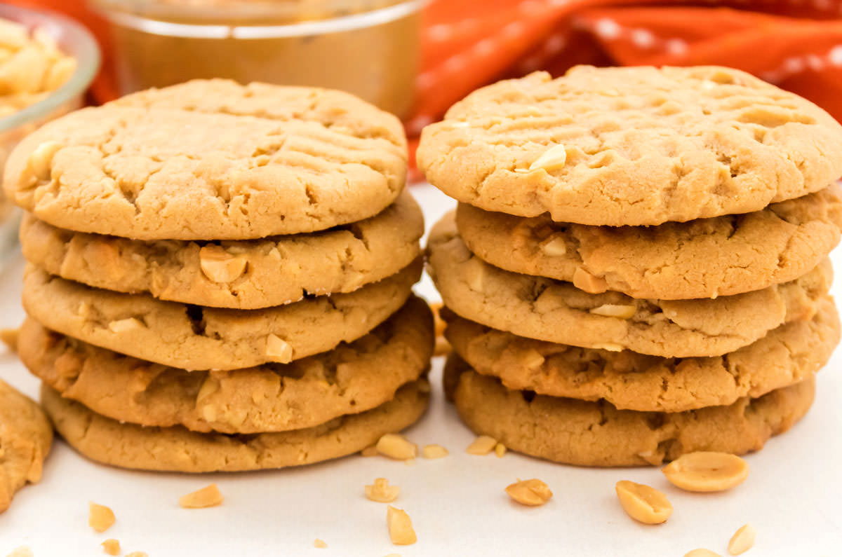 Closeup on two stacks of Chunky Peanut Butter Cookies sitting on a white table surrounded by chopped peanuts.