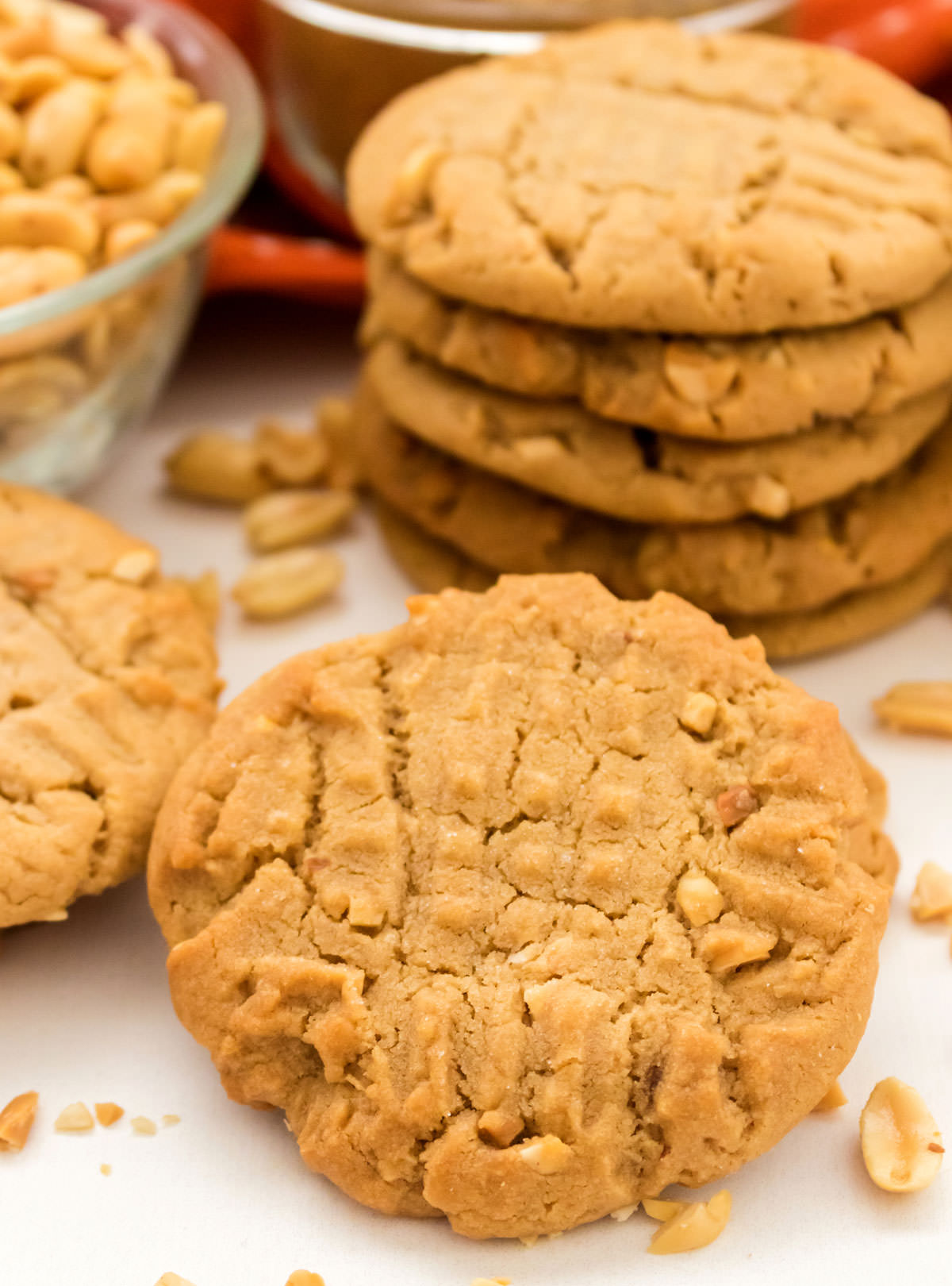 Closeup on a Chunky Peanut Butter Cookie surrounded by peanuts sitting in front of stacks of more cookies.