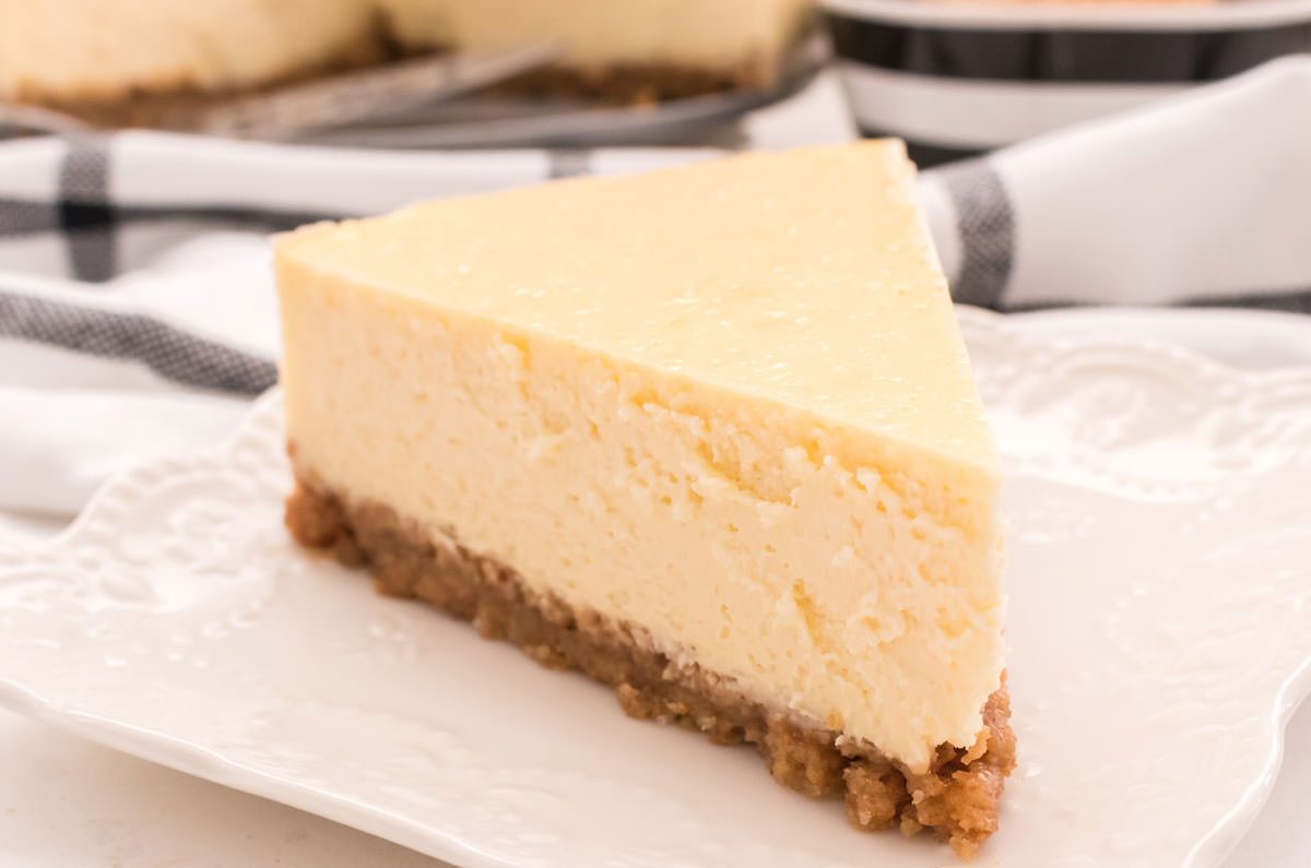 A closeup on a slice of cheesecake sitting on a white plate in front of a black and white table linen.